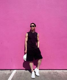 a man standing in front of a pink wall with his hands on his hips and wearing sunglasses