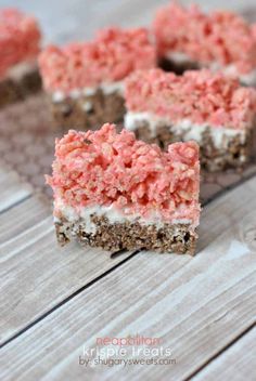 several pieces of cake with pink and white frosting on them sitting on a wooden table