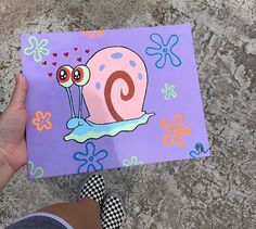 a hand holding up a purple card with a snail on it's side and flowers in the background