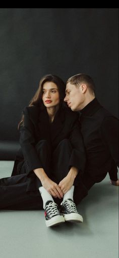 a man and woman sitting on the ground with their arms around each other's shoulders