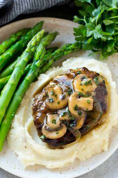 a plate with mashed potatoes, mushrooms and asparagus on it next to some greens