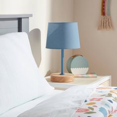 a bed with white sheets and a blue lamp next to it on top of a nightstand