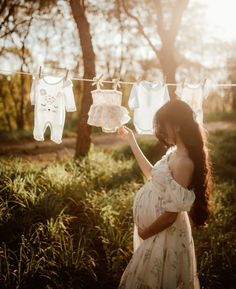 a pregnant woman is looking at clothes hanging on a line