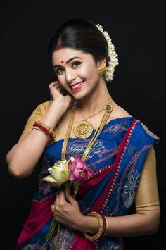 a woman in a blue and red sari holding a flower on her left hand