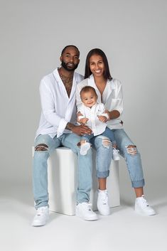 a man and woman sitting on top of a white cube with a baby in their lap