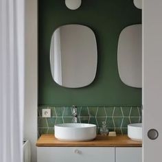 a bathroom with two round mirrors above the sink and green wall tiles on the walls