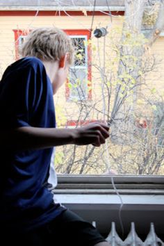 a boy sitting on a window sill looking out the window