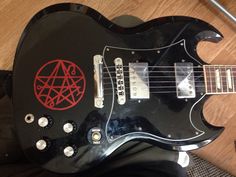 a black electric guitar with red pentagram on it's body sitting on a wooden floor