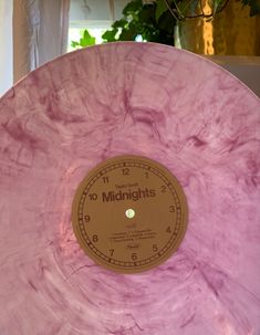 a large pink clock sitting on top of a wooden table next to a potted plant