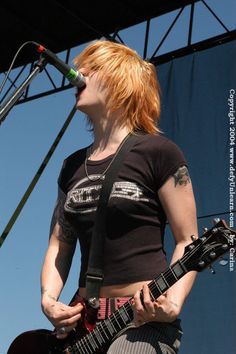 a woman with red hair and piercings playing an electric guitar at a music festival