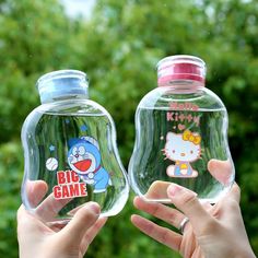 two people holding up hello kitty and big game water bottles