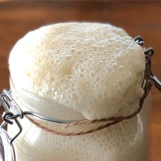 a glass jar filled with liquid sitting on top of a wooden table next to a metal wire