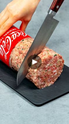 a person cutting meat with a large knife on top of a black board next to a can of coca - cola