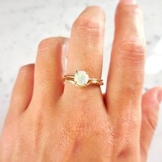 a woman's hand wearing a gold ring with an opal stone in it