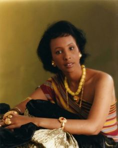 a woman wearing a necklace and bracelet sitting on the ground with her hand on her hip