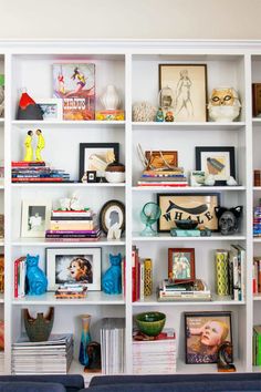 a living room filled with lots of books and pictures on top of white shelving