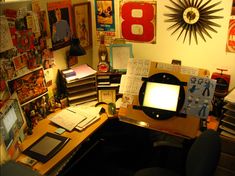 a desk with a computer on top of it next to a wall covered in posters