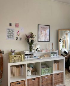 a white shelf filled with lots of books and baskets next to a wall mounted mirror