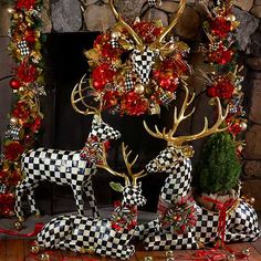 two deer statues sitting on top of a wooden floor next to a fire place covered in christmas decorations