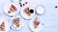 three slices of pie on plates with cherries and whipped cream in the bowl next to them