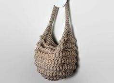 a crocheted bag hanging on the wall next to a white hanger with a button