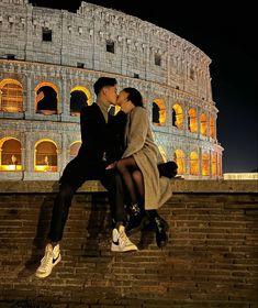 a man and woman kissing in front of the colossion at night, rome