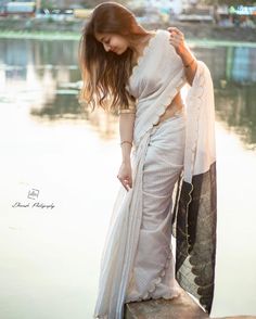 a woman in a white sari standing by the water