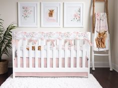 a white crib with pink bedding and pictures on the wall