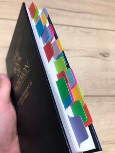 a person holding a book with colored papers on it