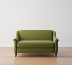 a green couch sitting on top of a hard wood floor next to a white wall