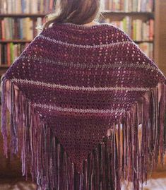 a woman wearing a purple crocheted shawl in front of a bookshelf