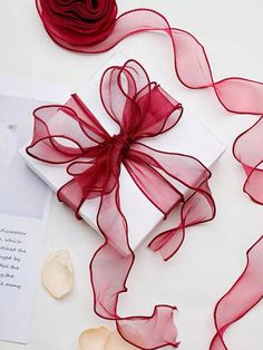 a red ribbon is tied on top of a white box and some flowers are next to it