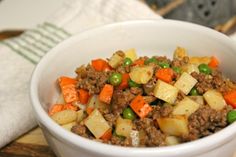 a white bowl filled with meat and veggies on top of a wooden cutting board