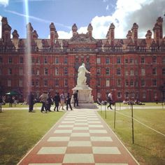 people are standing in front of a large building with a giant chess board on the lawn