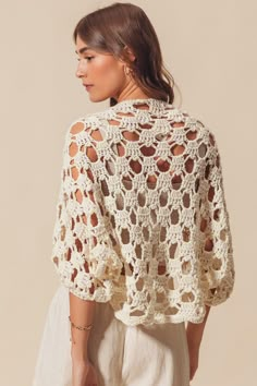 a woman wearing a white crocheted sweater with openwork on the shoulders and back