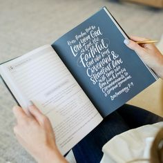 a woman is holding a book and writing on it with a pen in her hand