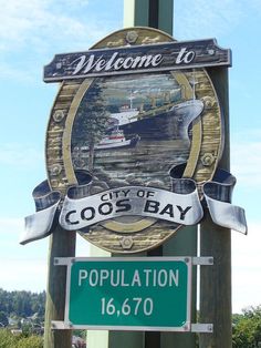 a welcome sign for the city of coos bay, with a boat in the background