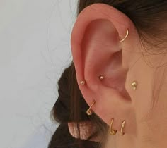 a woman wearing three different ear piercings on her left ear and the other one is gold