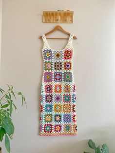 a crocheted dress hanging on a wall next to a potted green plant