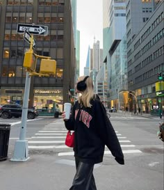 a woman walking across a street holding a cup in one hand and a cell phone in the other