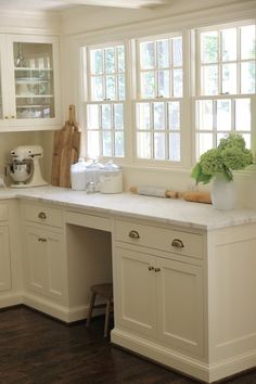 a kitchen with white cabinets and counter tops next to a window filled with potted plants