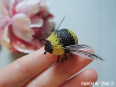 a tiny yellow and black bee sitting on top of a persons hand next to flowers