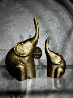 two gold elephants are on display in a glass case with a tag hanging from it's ear