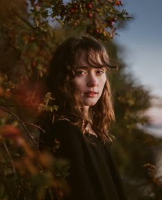 a woman standing in front of an apple tree looking at the camera with a serious look on her face