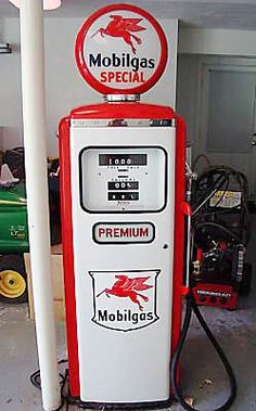 a red and white gas pump sitting in a garage next to a green tractor with the word mobbilgas special written on it