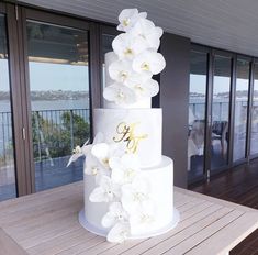 a three tiered white wedding cake with orchids on the bottom and gold monogramming