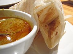 a bowl of soup and some pita bread on a plate with dipping sauce in it