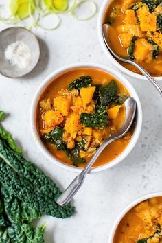 three bowls of soup with spinach and other vegetables on the table next to it