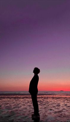 a man standing on top of a beach next to the ocean at sunset or dawn