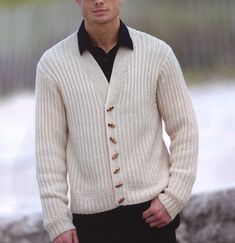 a man wearing a white cardigan and black shirt standing in front of a lake